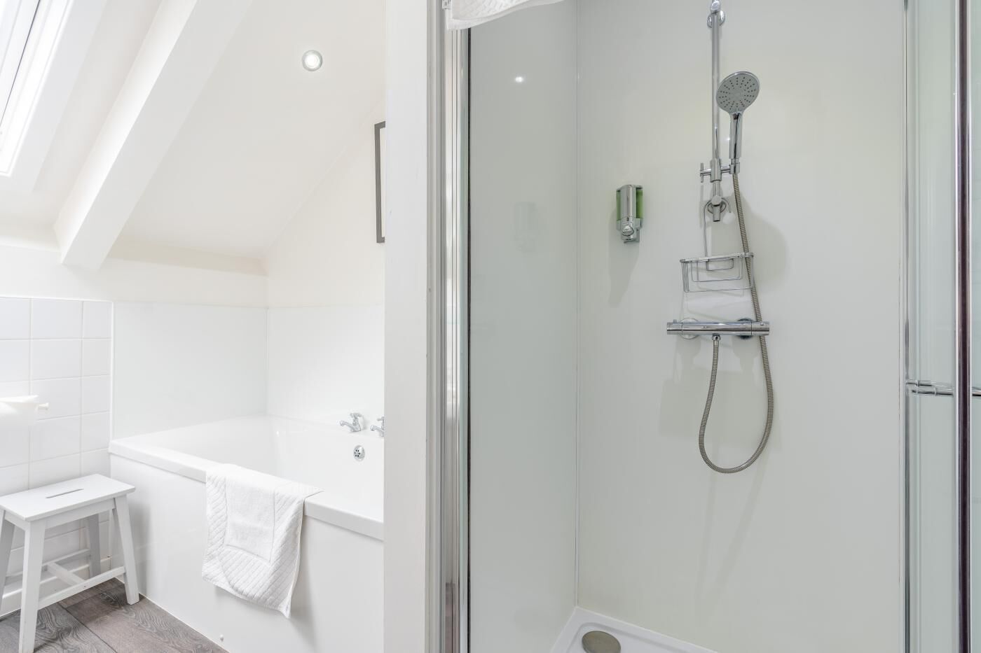 Une salle de bain moderne avec une douche à parois de verre, une baignoire blanche et un petit meuble-lavabo agrémenté d’une serviette.