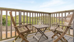 Terraza de madera con dos sillas y una mesa, con vistas a una zona verde con colinas.