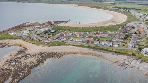 Un pueblo costero con playa, casas y un muelle.