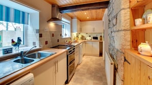 A modern kitchen with wooden beams, a stone wall, and a window with a view. - 2 Bed in Belford (oc-79885) (Belford)