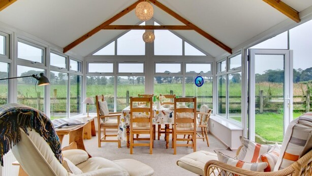 A conservatory with a dining table and chairs, large windows, and a view of the countryside. - 2 Bed in Belford (oc-79885) (Belford)
