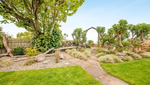 Un giardino curato con vialetto in pietra, un gazebo in legno e diverse piante e alberi.