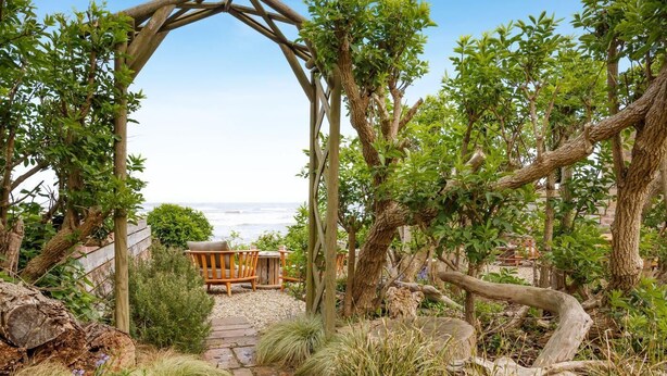 Una pergola in legno con panchina e tavolo, immersa nel verde e con vista sulla spiaggia.