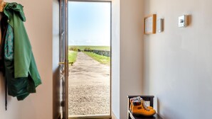 Una habitación con una puerta que da a un camino de grava, un perchero con una chaqueta verde, un par de botas y un termostato fijado a la pared.