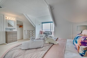 A bedroom with a bed, a dresser, a vanity, a window, and a ceiling light.