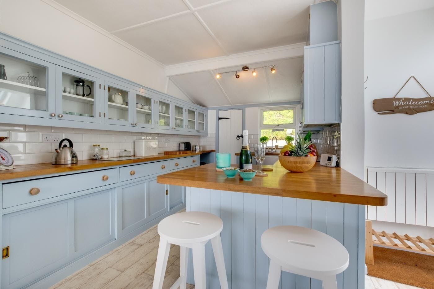 A kitchen with light blue cabinets, a wooden countertop, and two white stools.