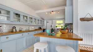 Una cocina con armarios azul claro, encimera de madera y dos taburetes blancos.