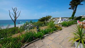 Un jardín con un sendero de piedra que lleva a un espacio de descanso con vistas al mar.