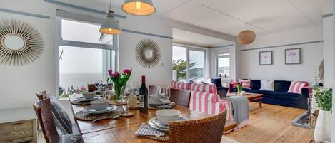 Un amplio salón con una mesa de comedor preparada para una comida, un sofá y vistas al exterior.