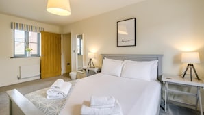 A hotel room with a large bed, two bedside tables with lamps, a framed picture on the wall, a window with curtains, and a radiator. - 4 Bed in Mundesley (oc-1983) (Mundesley)