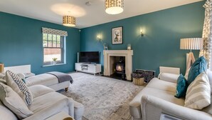 A living room with teal walls, a fireplace, a television, and two sofas. - 4 Bed in Mundesley (oc-1983) (Mundesley)