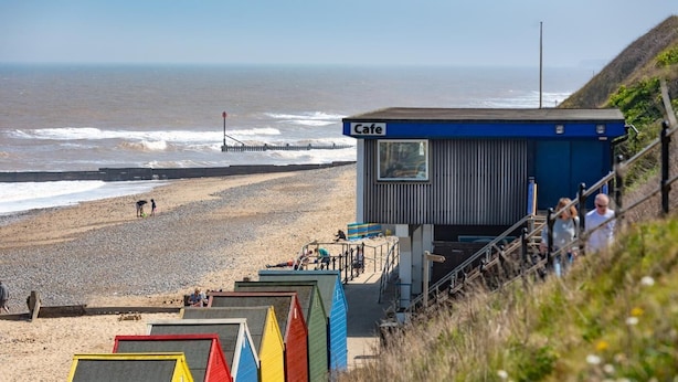 A beachside cafe with a view of the ocean, a staircase leading down to beach huts, and a lifeguard tower in the background. - 4 Bed in Mundesley (oc-1983) (Mundesley)