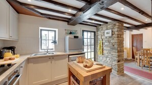 Una cocina moderna con armarios blancos, un pilar de piedra y vigas de madera.
