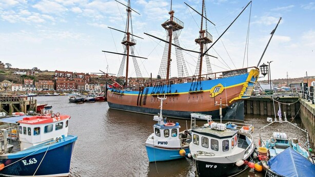 Ein großes Segelschiff liegt im Hafen, in der Nähe befinden sich kleinere Boote.