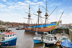 Um grande navio a vela atracado num porto, com embarcações menores por perto.