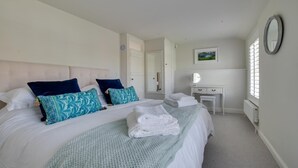 A bedroom with a large bed, white walls, a bedside table with a mirror, and a window with blinds. - 4 Bed in Southwold (oc-hilsi) (Southwold)
