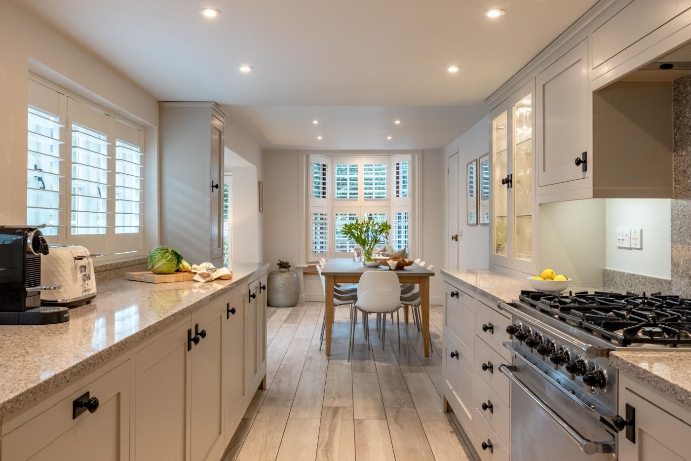 Une cuisine moderne avec un coin repas, comprenant une cuisinière à gaz, des placards et une fenêtre avec des stores.