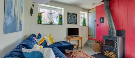 Ein gemütliches Wohnzimmer mit einem blauen Sofa, einem Fernseher, einem Kamin und einer roten Wand.