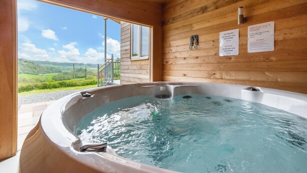 A hot tub in a wooden cabin with a view of the countryside.