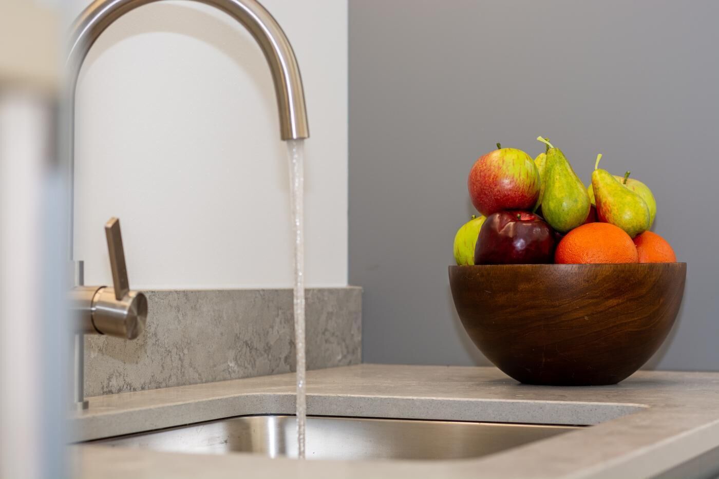 Een moderne keukenkraan met een roestvrijstalen hendel en een houten kom vol fruit.