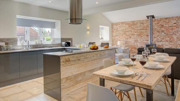 Una cocina moderna con una isla central, un área de comedor con pared de ladrillo y una chimenea grande.