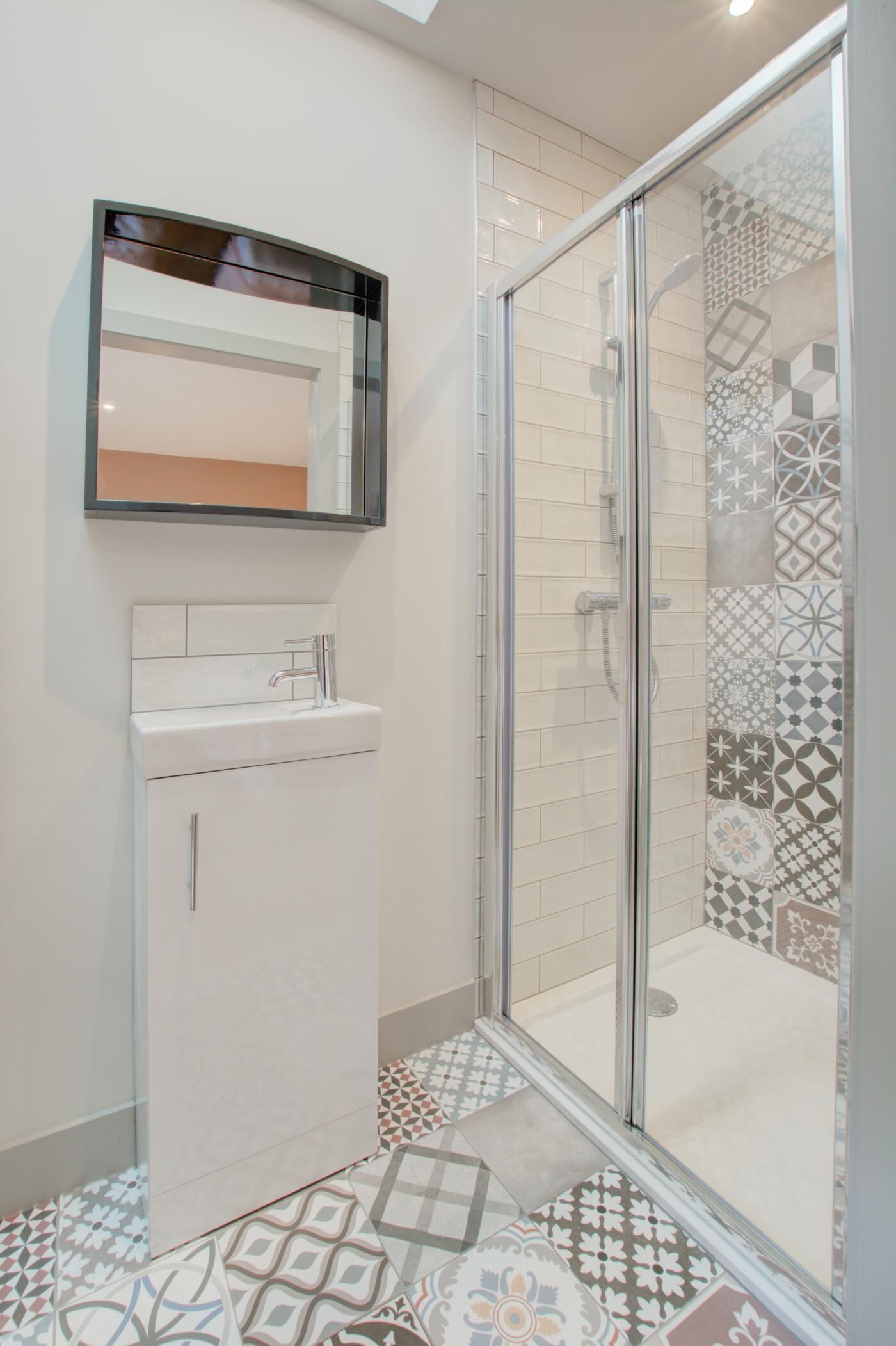 Une salle de bain avec un lavabo blanc, un miroir et une douche aux carreaux décorés.