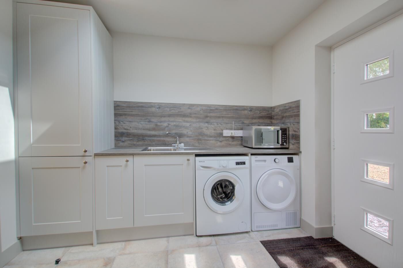 A laundry room with a washing machine, dryer, microwave, and a sink.