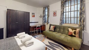 Ein kleiner Raum mit einem Bett, einer grünen Schlafsofa, einem Schreibtisch und einem Kleiderschrank.