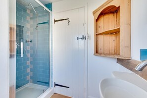 A bathroom with a glass-enclosed shower, a white door, and a wooden medicine cabinet above a sink.