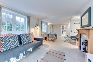 Un salon moderne avec un canapé, une table à manger et des chaises. On y trouve une cheminée et une vue sur l’extérieur grâce à de grandes fenêtres.