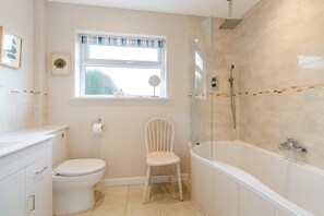A bathroom with a toilet, a chair, a bathtub, and a shower enclosure.