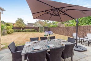 An outdoor patio with a table set for dining, surrounded by wicker chairs, under a large umbrella.