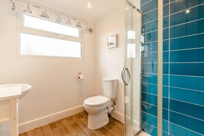 Ein Badezimmer mit Toilette, Waschbecken, Fenster und einer blauen Duschkabine.