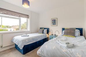 A bedroom with two beds, a window, a radiator, and a nightstand with lamps.