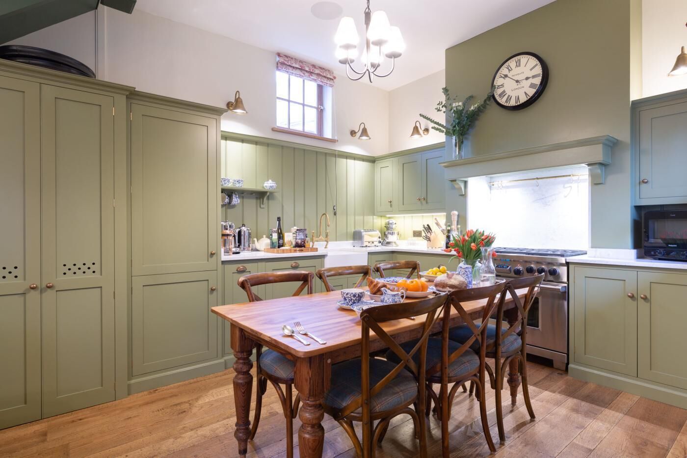 Una cocina con armarios verdes, una mesa de comedor de madera y un reloj en la pared.