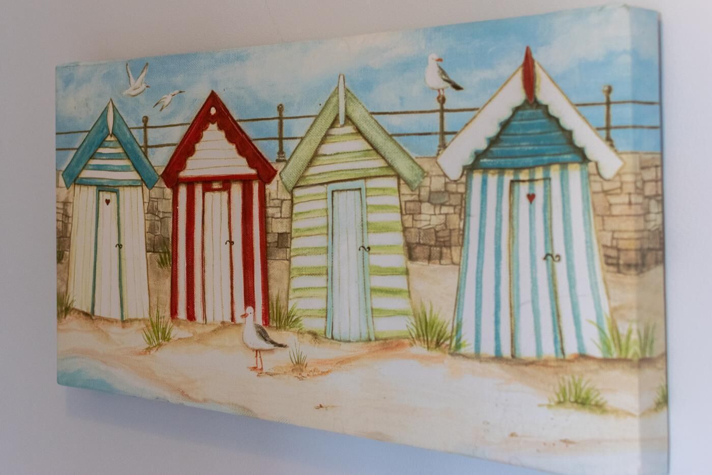 Une scène de bord de mer avec trois cabanes de plage rayées et un goéland.
