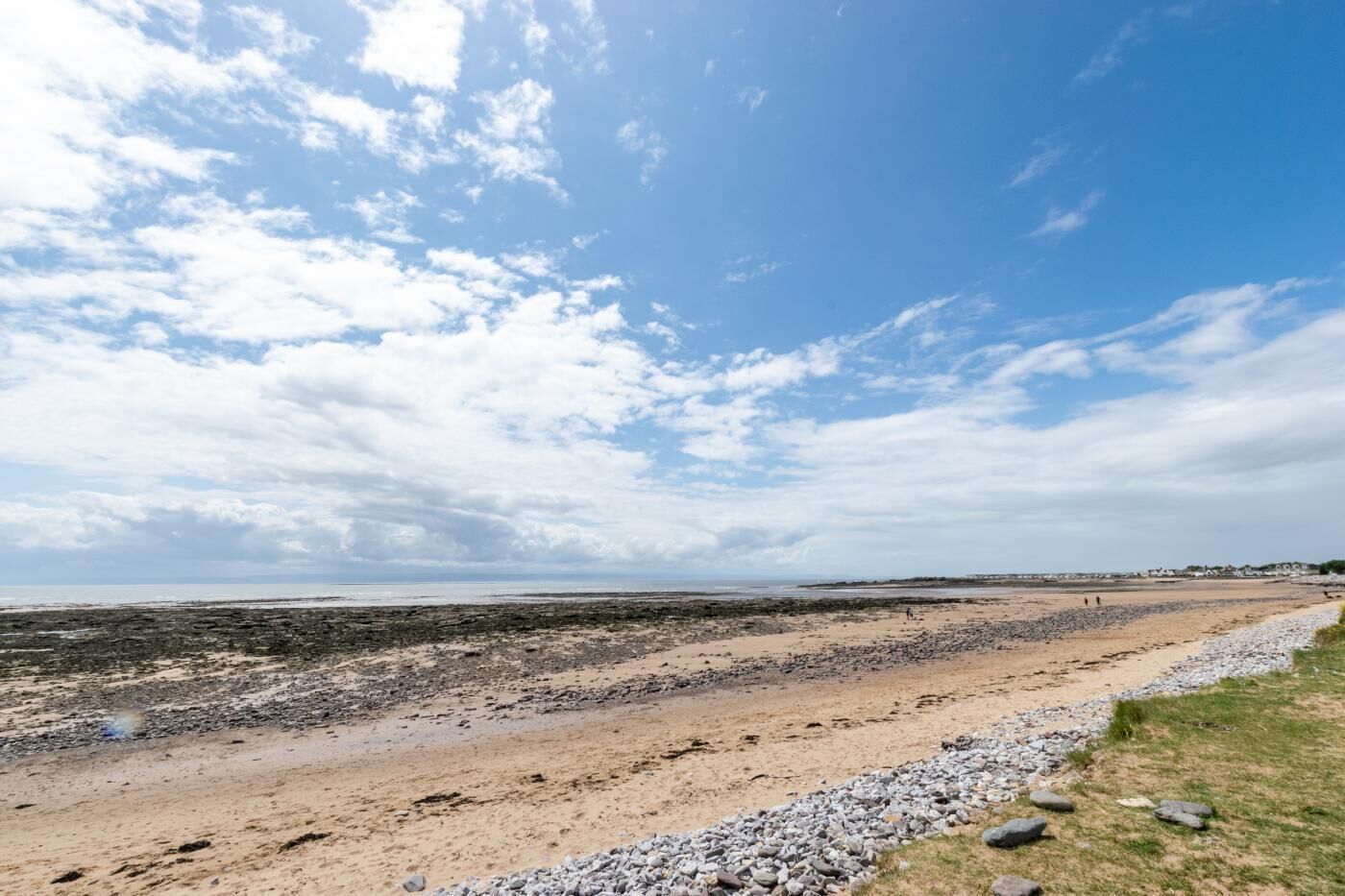 A coastal beach with a wide sandy area, rocky shoreline, and a clear sky.