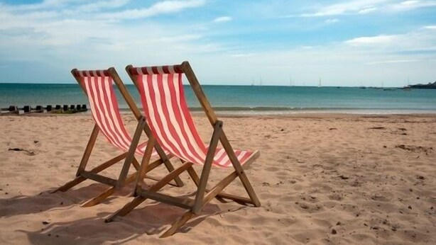 Two striped beach chairs on a sandy beach with a clear sky and calm sea in the background.