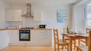 A modern kitchen with white cabinetry, a built-in oven, a microwave, and a dining area with wooden chairs and a table set for two.