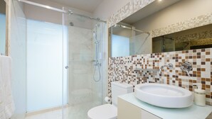 A modern bathroom with a glass-enclosed shower, a white toilet, and a sink with a mosaic backsplash. - Extendall 1 in Oporto (Porto)