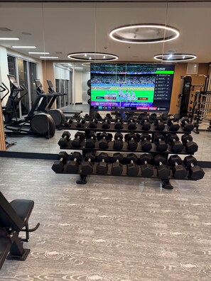 A gym with treadmills, a TV displaying a sports game, and a rack of dumbbells. - 2-bedroom apartment in lovely Daytona Beach with AC  for Corporate Housing only. (Daytona Beach)
