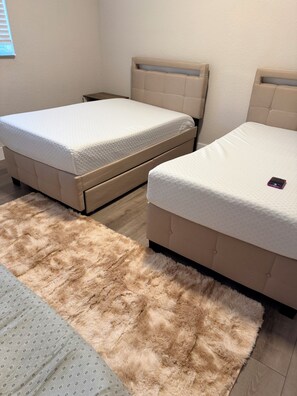 Two beds with beige headboards and white bedding, a fluffy beige rug, and a patterned rug. - 2-bedroom apartment in lovely Daytona Beach with AC  for Corporate Housing only. (Daytona Beach)