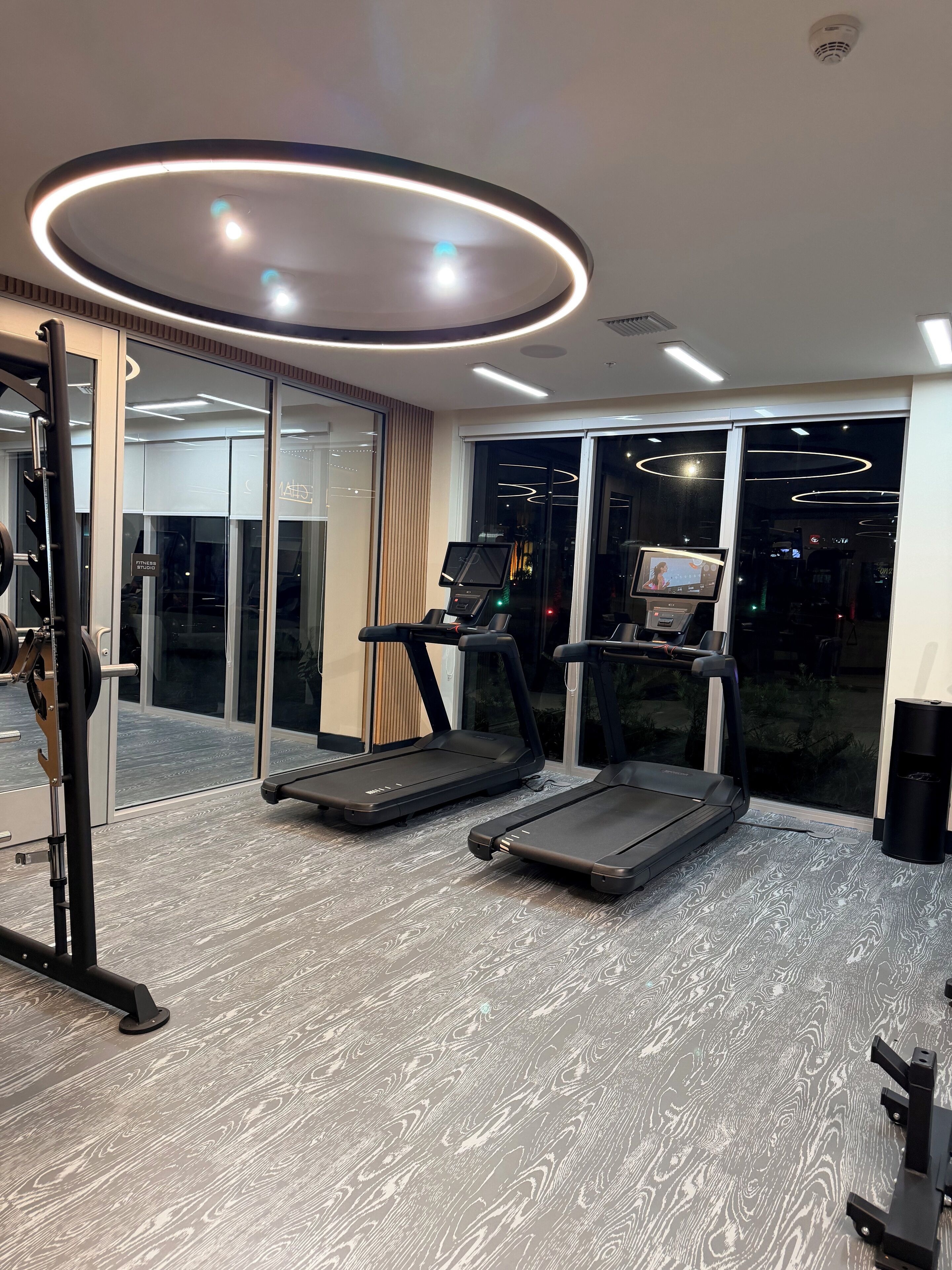Ein modernes Fitnessstudio mit Laufbändern, einer Gewichtbank und einem digitalen Bildschirm.