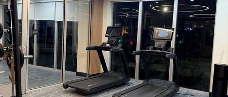 A modern gym with treadmills, a weight bench, and a digital display.