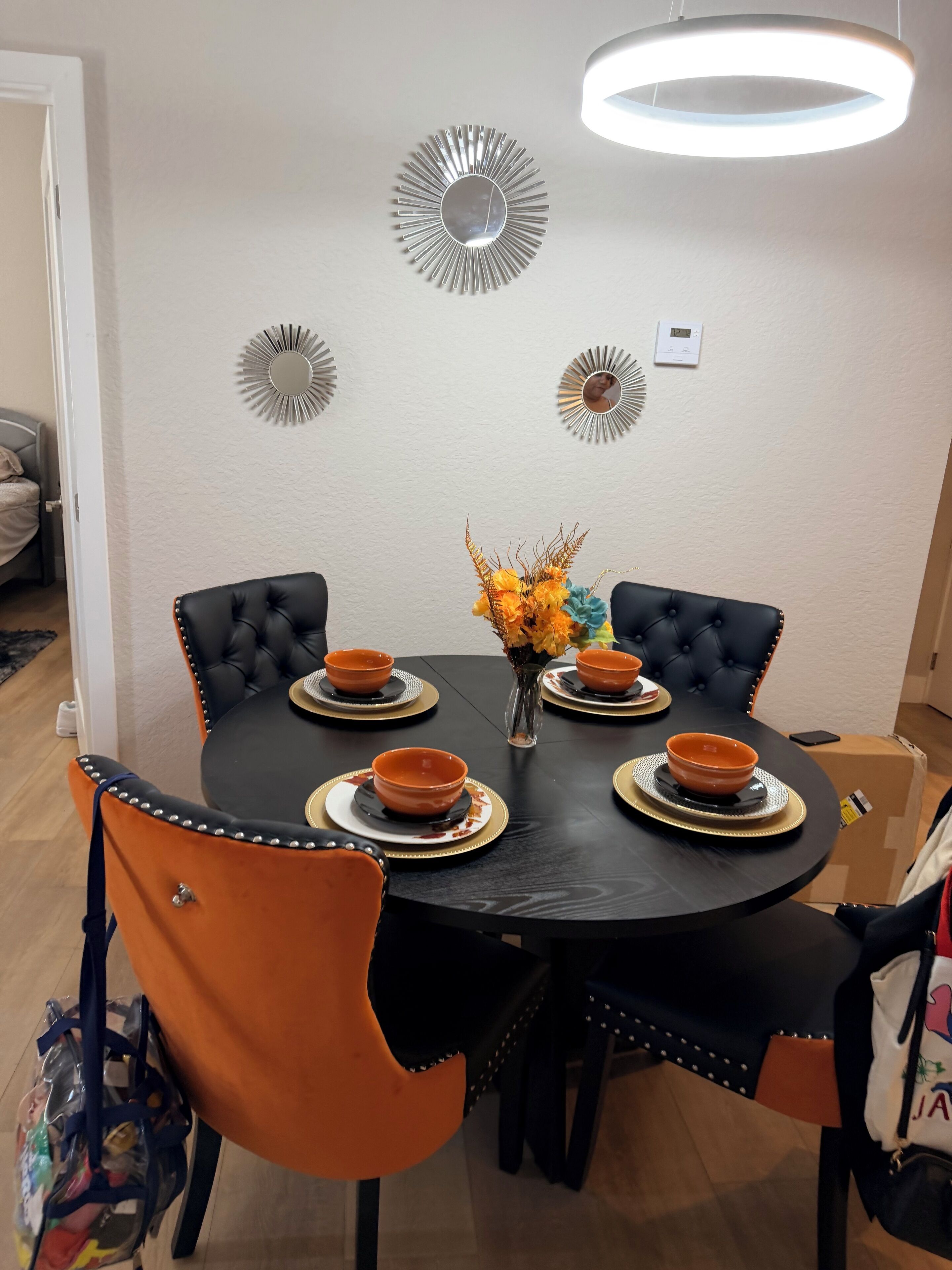 A dining area with a round table, black and orange chairs, and a vase with flowers.