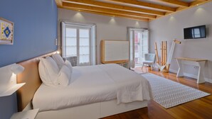 Ein Schlafzimmer mit einem großen Bett, Holzbalken, einem Fernseher und einem Schreibtisch mit Kunstmaterialien.
