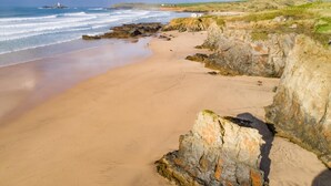 A coastal beach with rocky cliffs and a lighthouse in the distance. - 3 Bed in Trevone (oc-p00758) (Trevone)