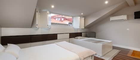 A bedroom with a bed, a bedside table, a chair, a window, and an air conditioning unit.