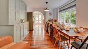 A spacious kitchen with wooden flooring, a dining table set for breakfast, and large windows providing natural light.