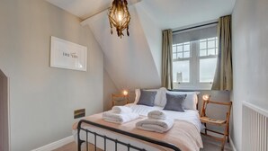 A bedroom with a bed, bedside tables, a chandelier, a window with curtains, and a framed picture on the wall.